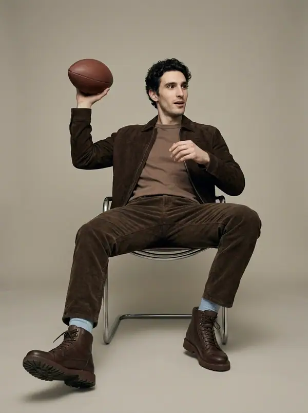 dark brown suede zip trucker + football prop worn by an AI male model, studio shoot